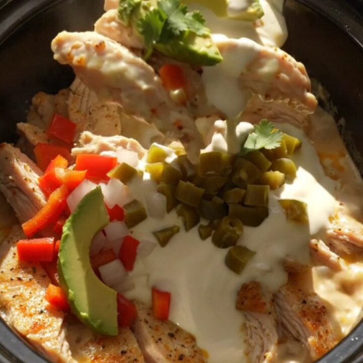 A close-up shot of creamy Pollo con Queso in a black slow cooker with bubbling white cheese.
