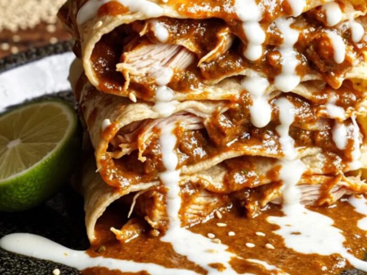 A tall, beautiful slice of chicken mole enchilada stack served on a plate with fresh garnishes.