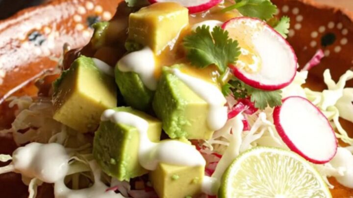 A steaming bowl of red pork posole topped with fresh cilantro, radish slices, and avocado in a rustic clay bowl.