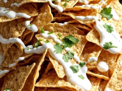 A close-up shot of a slow cooker filled with bubbling, cheesy carnitas dip garnished with cilantro and lime.