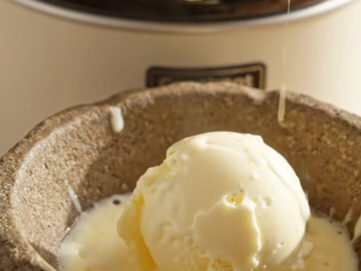 A close-up of a serving of warm peach dump cake in a stoneware bowl with melting vanilla ice cream on top.
