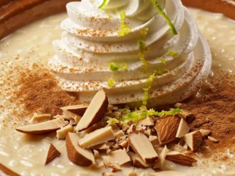 A close-up of creamy Tres Leches Horchata Rice Pudding in a stoneware bowl topped with dulce crema and almonds.