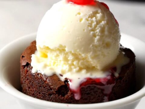 A close-up of a dark chocolate cherry dump cake in a black stoneware slow cooker with a spoon lifting a portion.