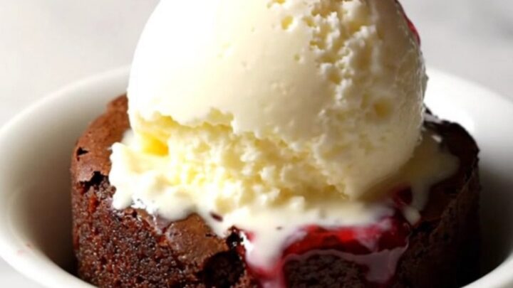 A close-up of a dark chocolate cherry dump cake in a black stoneware slow cooker with a spoon lifting a portion.