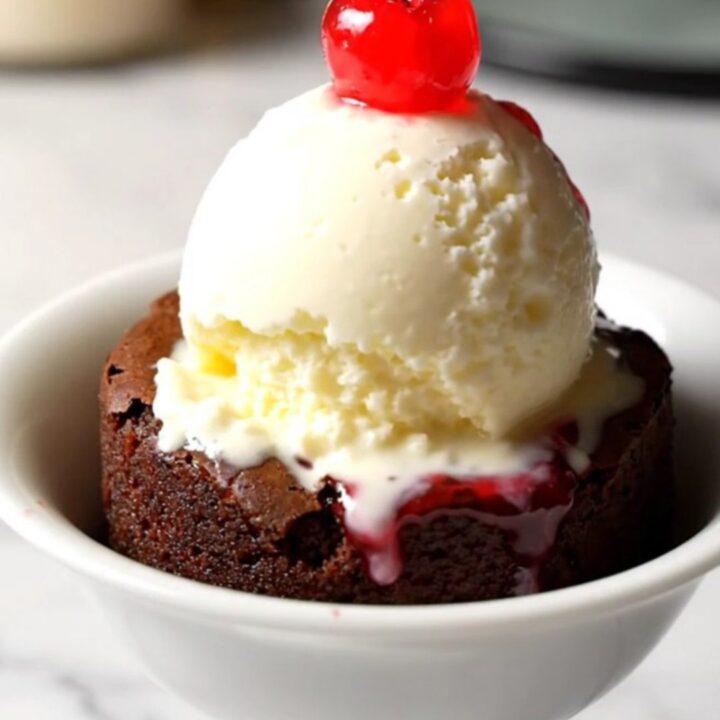 A close-up of a dark chocolate cherry dump cake in a black stoneware slow cooker with a spoon lifting a portion.