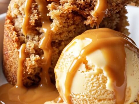 A warm, golden caramel apple dump cake in a glossy cinnamon-red Crockpot, scooped into a white ceramic dish.