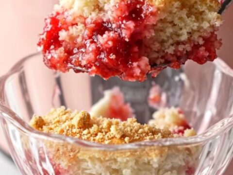 A close-up shot of a strawberry cheesecake dump cake in a blush-pink Crockpot with steam rising.