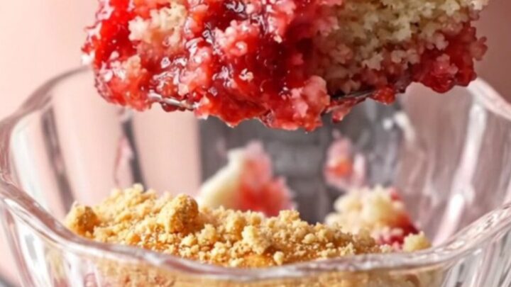 A close-up shot of a strawberry cheesecake dump cake in a blush-pink Crockpot with steam rising.