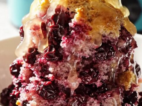 A vibrant lemon blueberry dump cake served in a ceramic bowl, showing purple berries and golden crust.