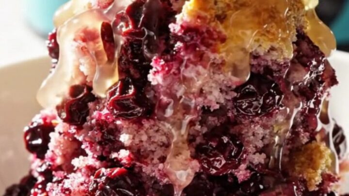 A vibrant lemon blueberry dump cake served in a ceramic bowl, showing purple berries and golden crust.