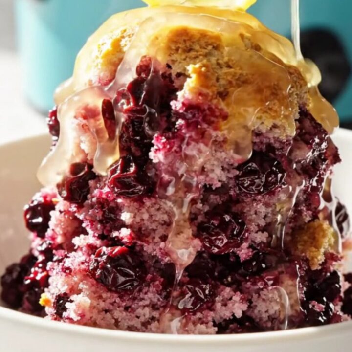 A vibrant lemon blueberry dump cake served in a ceramic bowl, showing purple berries and golden crust.