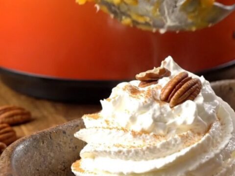 A warm, golden pumpkin pecan crunch cake served in a stoneware dish with whipped cream.