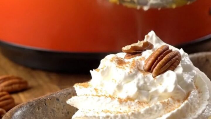 A warm, golden pumpkin pecan crunch cake served in a stoneware dish with whipped cream.