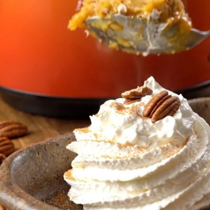 A warm, golden pumpkin pecan crunch cake served in a stoneware dish with whipped cream.
