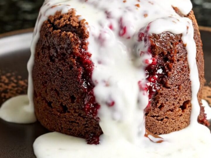 A steaming scoop of rich chocolate raspberry cake in a dark bowl with a dusting of cocoa and cream.