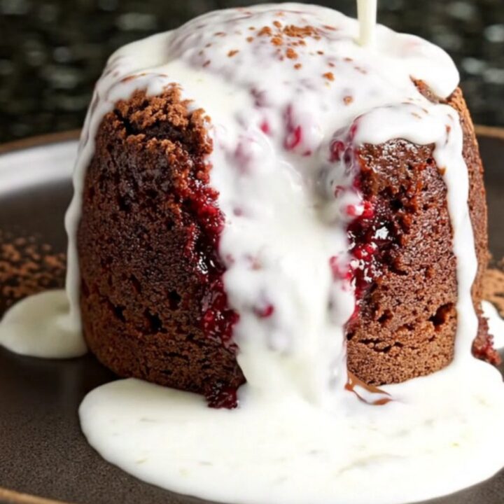 A steaming scoop of rich chocolate raspberry cake in a dark bowl with a dusting of cocoa and cream.