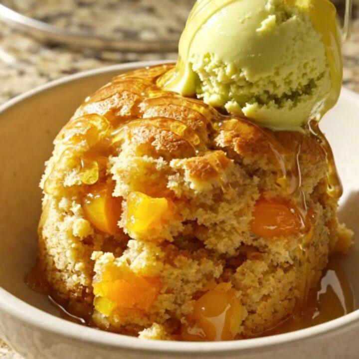 A warm, golden apricot honey almond dump cake served in a shallow bowl with a scoop of pistachio gelato on top.