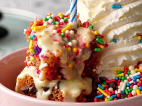 A warm, gooey Funfetti dump cake inside a ceramic slow cooker with rainbow sprinkles.