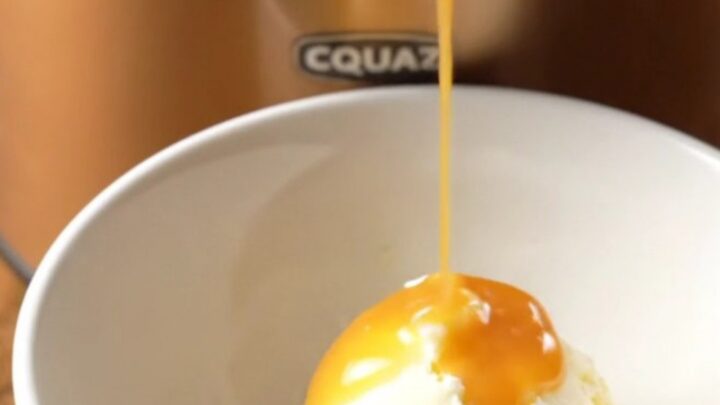 A close-up of a warm butterscotch pecan pudding cake in a crockpot with a spoon scooping out a piece.