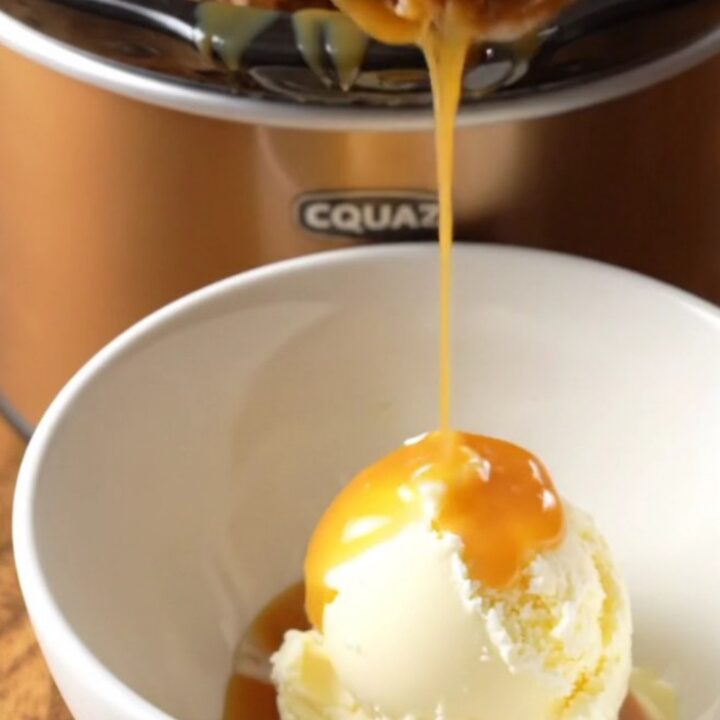 A close-up of a warm butterscotch pecan pudding cake in a crockpot with a spoon scooping out a piece.