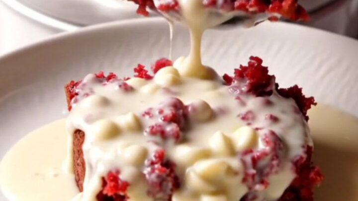 A close-up view of a red velvet lava cake in a white ceramic slow cooker with a spoon lifting a molten center.
