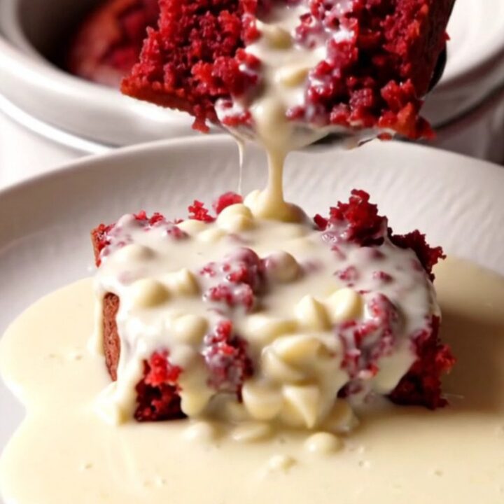 A close-up view of a red velvet lava cake in a white ceramic slow cooker with a spoon lifting a molten center.