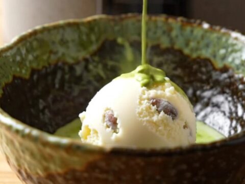 A warm bowl of matcha molten lava cake with a scoop of vanilla ice cream on a wooden table.
