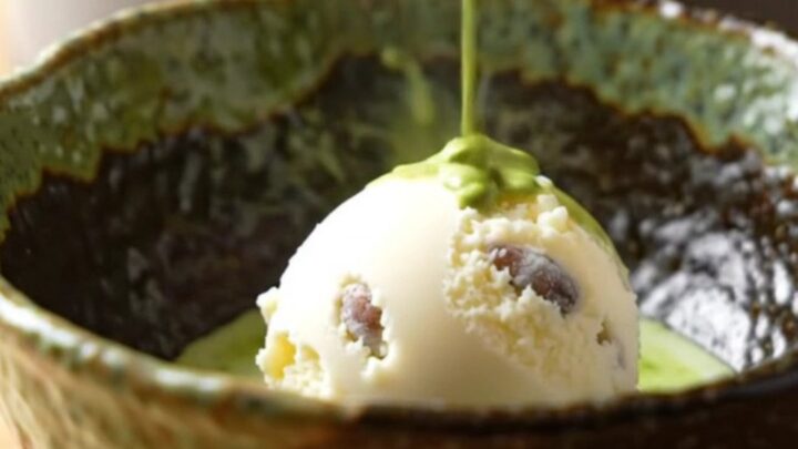 A warm bowl of matcha molten lava cake with a scoop of vanilla ice cream on a wooden table.