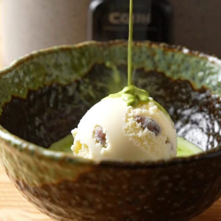 A warm bowl of matcha molten lava cake with a scoop of vanilla ice cream on a wooden table.