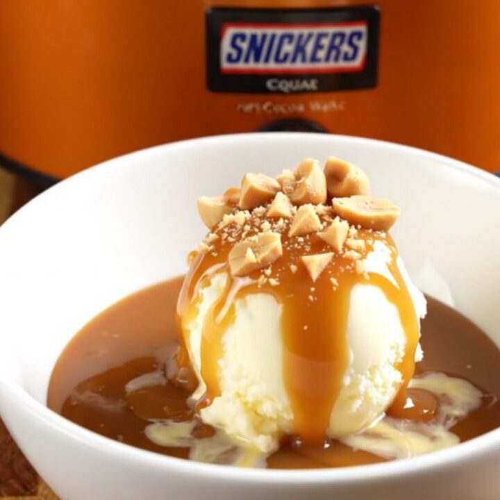 A warm Snickers lava cake in a slow cooker with a spoon scooping out a gooey, caramel-filled portion.