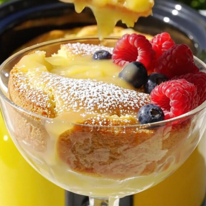 A warm, golden lemon butter cake in a yellow slow cooker with a pool of lemon curd sauce.