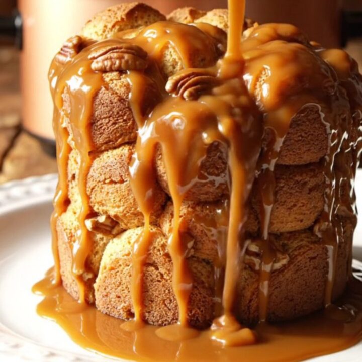 A close-up of pull-apart monkey bread with glossy caramel and toasted pecans in a rustic slow cooker.