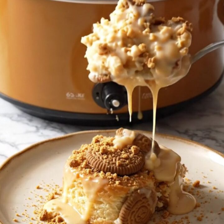 A close-up view of the Biscoff cinnamon roll casserole in a ceramic slow cooker with steam rising.