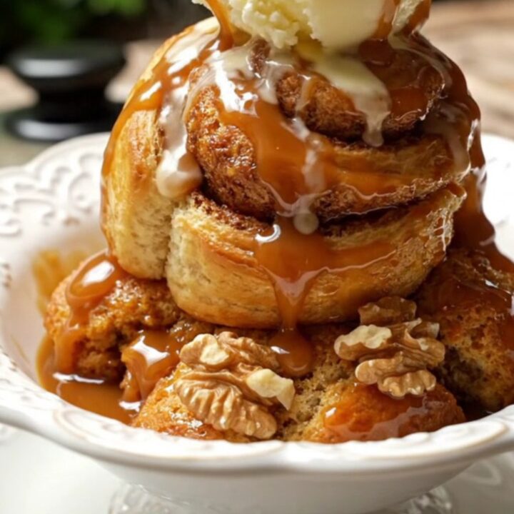 A steaming scoop of Bananas Foster cinnamon roll casserole topped with vanilla ice cream in a white bowl.