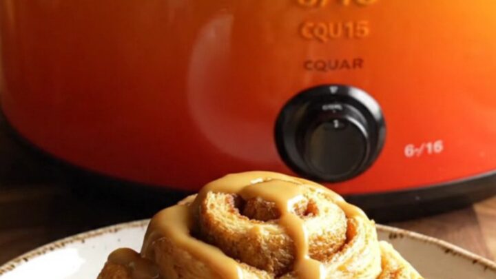 A golden, steaming pumpkin spice cinnamon roll casserole in a pumpkin-orange stoneware slow cooker.