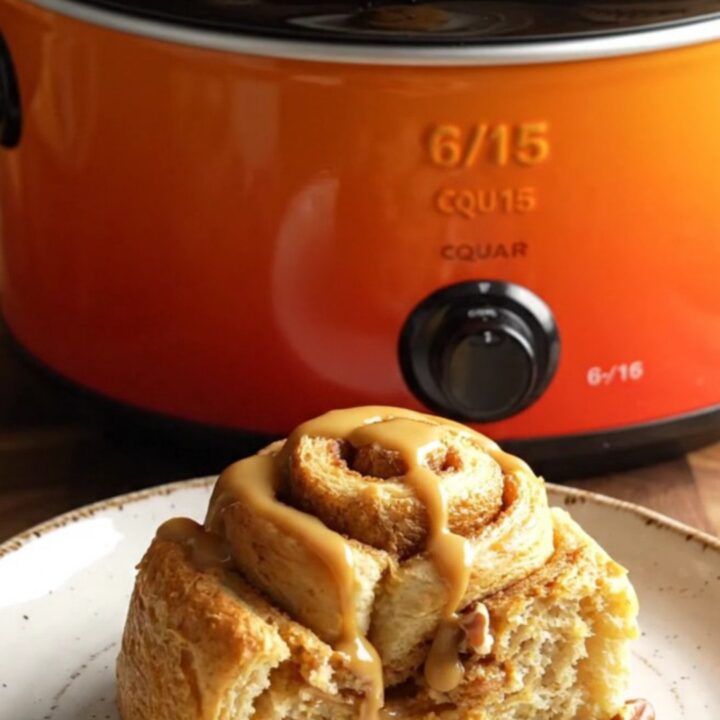 A golden, steaming pumpkin spice cinnamon roll casserole in a pumpkin-orange stoneware slow cooker.