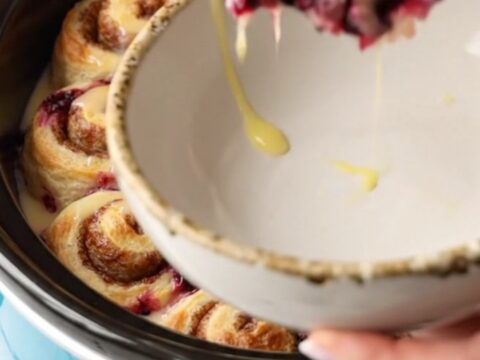 A ceramic blue slow cooker filled with a golden cinnamon roll and blueberry casserole.
