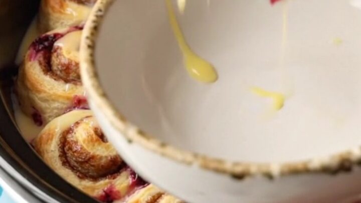 A ceramic blue slow cooker filled with a golden cinnamon roll and blueberry casserole.