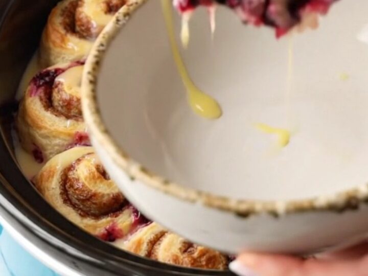 A ceramic blue slow cooker filled with a golden cinnamon roll and blueberry casserole.
