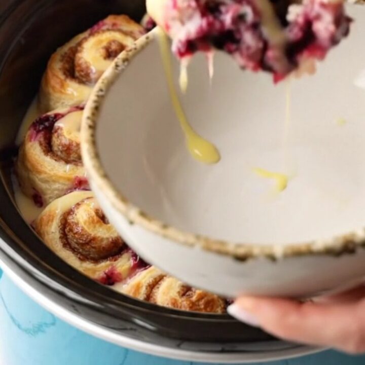 A ceramic blue slow cooker filled with a golden cinnamon roll and blueberry casserole.