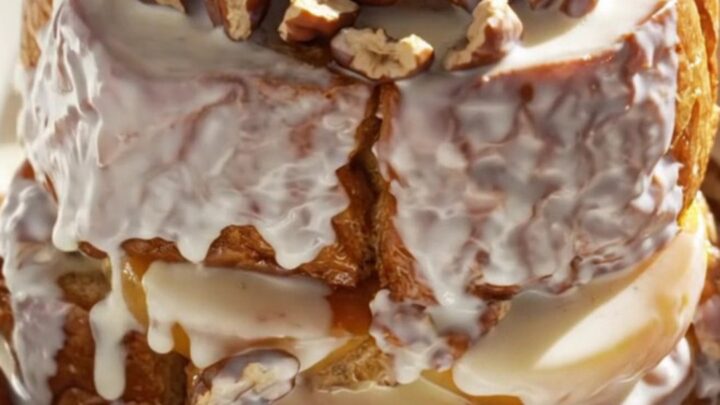 A golden, caramelized peach bourbon brioche French toast bake served in a shallow bowl with pecans.