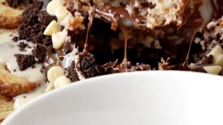 A close-up of a warm cinnamon roll and Oreo casserole in a black slow cooker with icing drizzled on top.