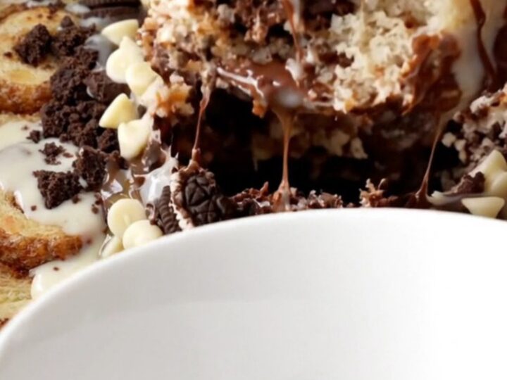 A close-up of a warm cinnamon roll and Oreo casserole in a black slow cooker with icing drizzled on top.