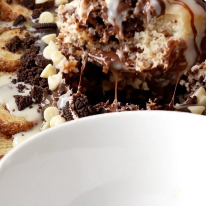 A close-up of a warm cinnamon roll and Oreo casserole in a black slow cooker with icing drizzled on top.