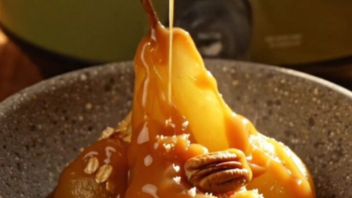 A close-up of a pear crisp in a stoneware bowl with salted caramel drizzled on top.