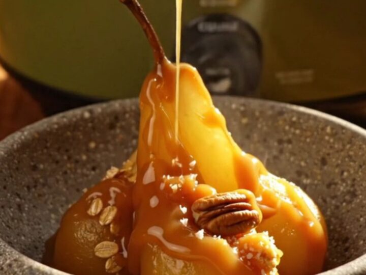 A close-up of a pear crisp in a stoneware bowl with salted caramel drizzled on top.