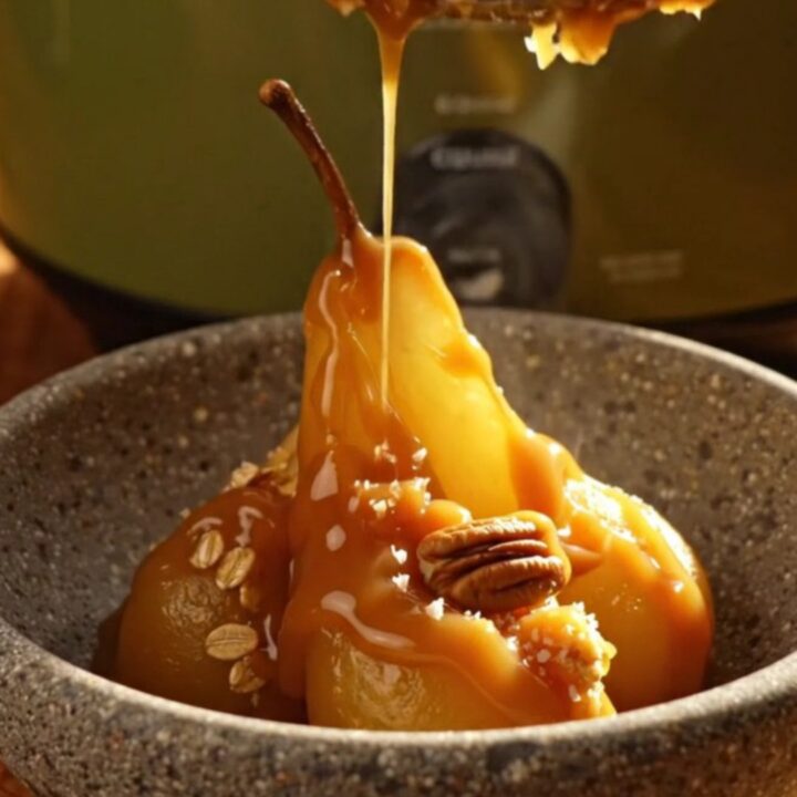A close-up of a pear crisp in a stoneware bowl with salted caramel drizzled on top.