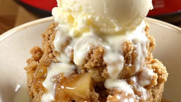 A steaming crockpot filled with tender Honeycrisp apple wedges under a golden, buttery oat crumble.