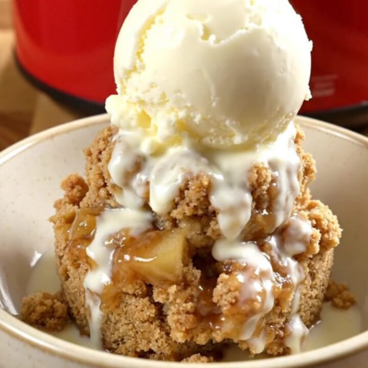 A steaming crockpot filled with tender Honeycrisp apple wedges under a golden, buttery oat crumble.