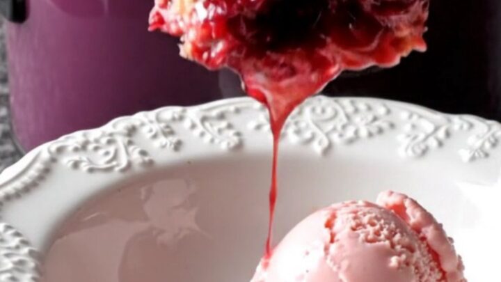 A dark plum ceramic slow cooker filled with a bubbling cherry crisp topped with a golden almond crumble.
